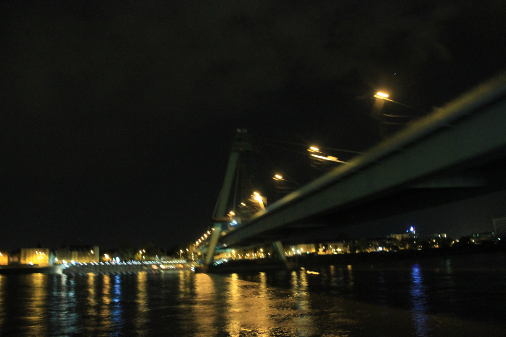 Sailing under a large bridge in Cologne, Germany at night