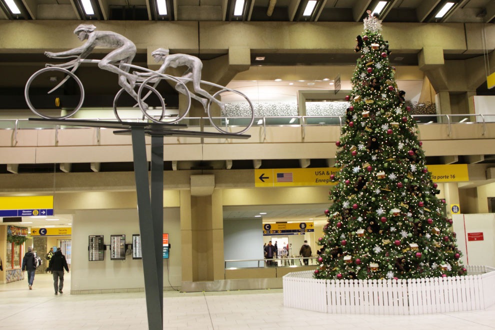 Sculpture of nude cyclists with a very large Christmas tree at YYC, Calgary airport