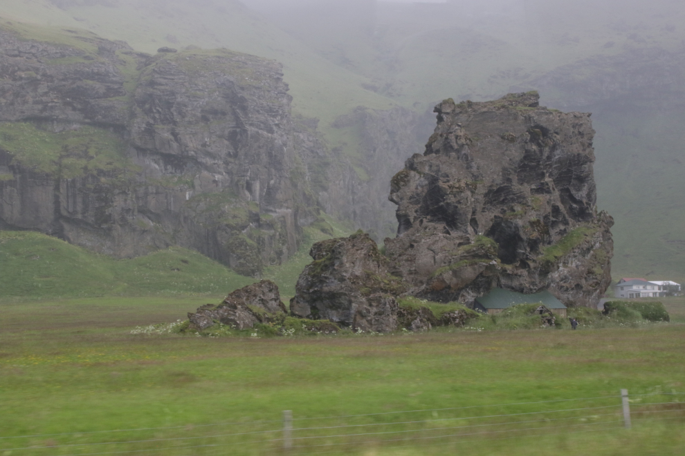 A stone house built into the base of a huge lava rock along Iceland Route 1.