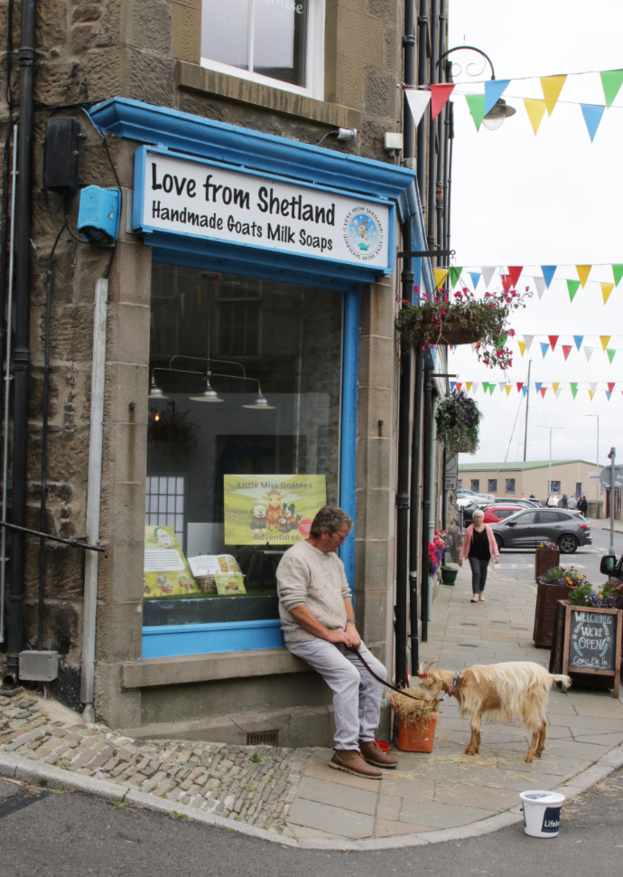 A man with a goat in front of a shop selling Handmade Goats Milk Soaps at Lerwick, Shetland.