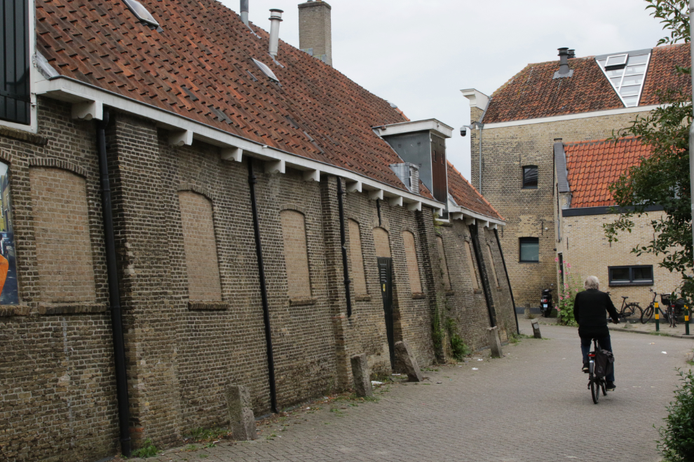 An old man on a bicycle rides by an old brick warehouse at Gouda, South Holland, the Netherlands.
