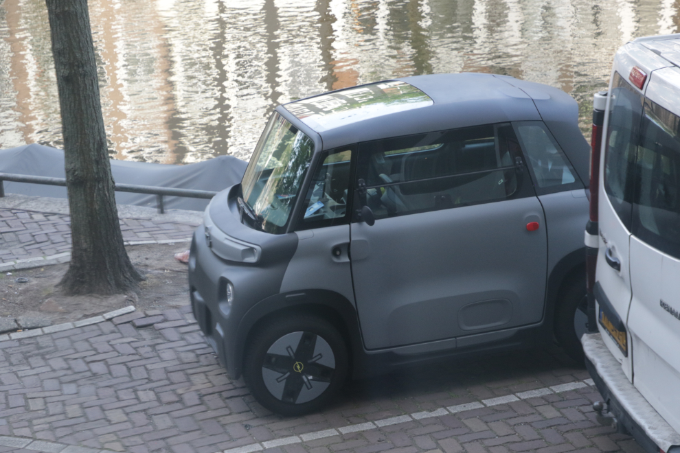 A tiny car parked beside a canal in Amsterdam.