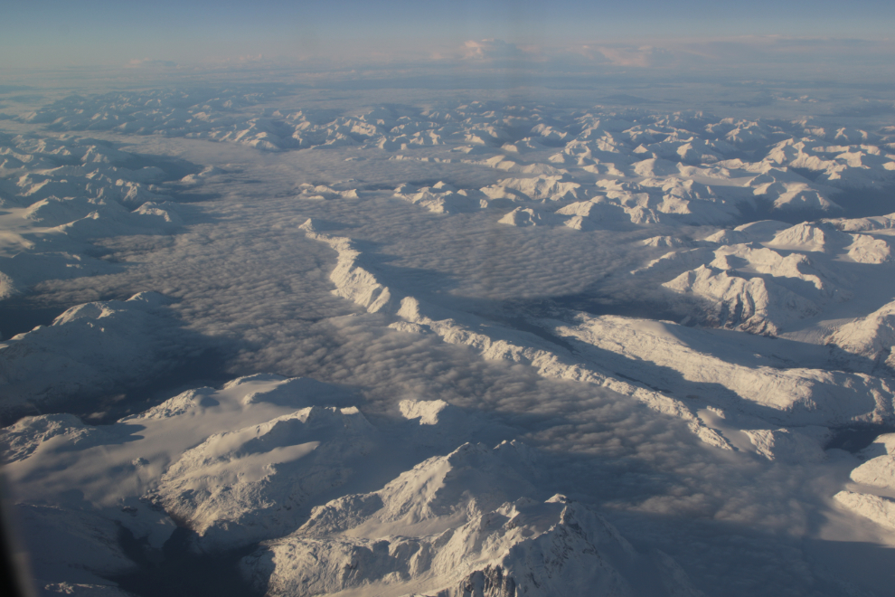 A sea of snowy mountains above a layer of low cloud and valley fog, between Whitehorse and Vancouver.